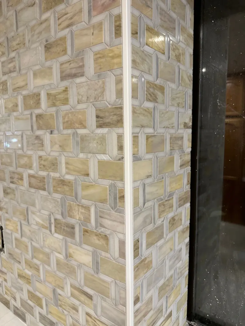 Cream, tan and gray mosaic pieces form an interlocking rectangular pattern around a corner beside a dark-framed opening.