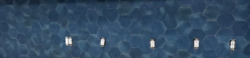 Deep blue hexagonal tiles cover a kitchen backsplash, with several uncovered electrical outlets visible across the wall.