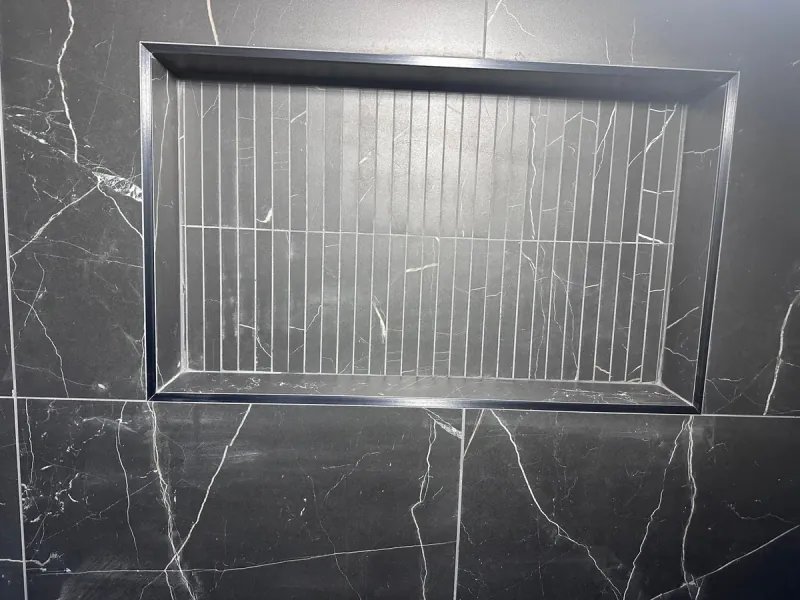 A recessed shower niche lined with narrow vertical tiles sits within dark, white-veined wall tile.