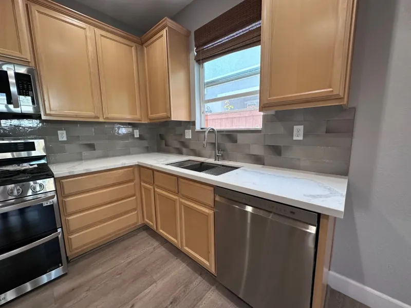 Gray rectangular backsplash tiles run in horizontal offset rows behind a kitchen counter and wrap around a window above the sink.