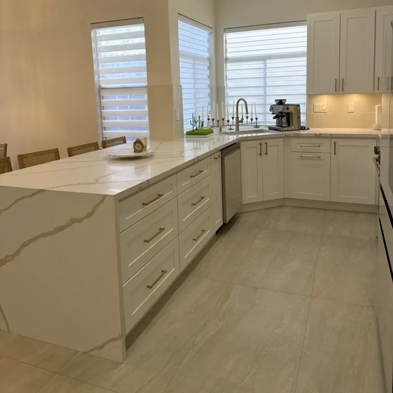 Pale rectangular floor tiles run beside white kitchen cabinets and a veined peninsula with a waterfall end.