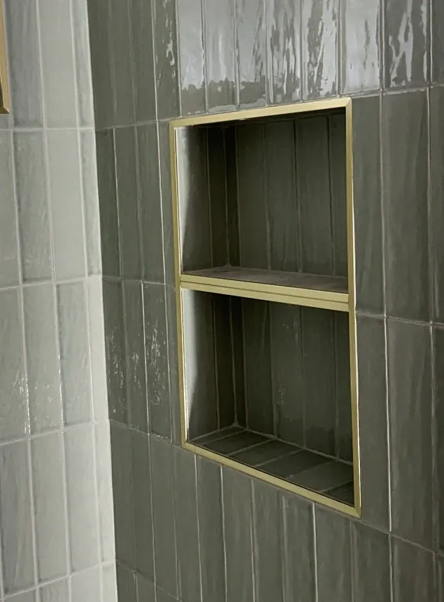 Two recessed storage compartments lined with gray-green vertical tile and outlined in gold-colored trim, separated by a tiled shelf.