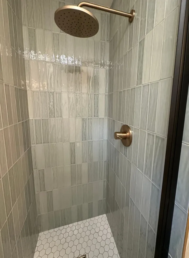 Glossy gray-green rectangular shower tiles set vertically with offset joints above a white hexagonal mosaic floor.