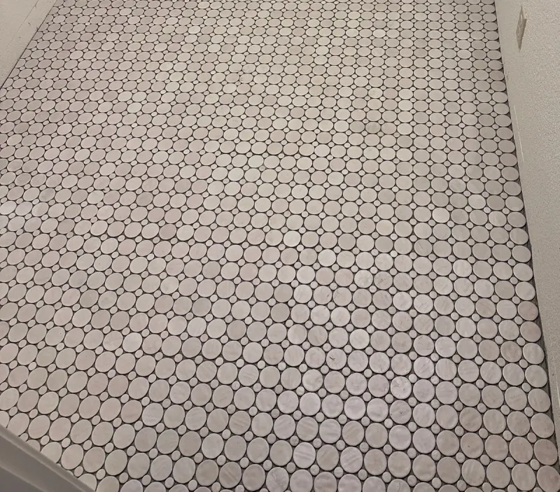 Pale circular tiles in two sizes form a repeating round-and-dot mosaic across a bathroom floor.