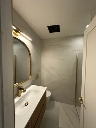 Pale veined wall and floor tile around a fluted vanity, warm-metal fittings and a toilet.