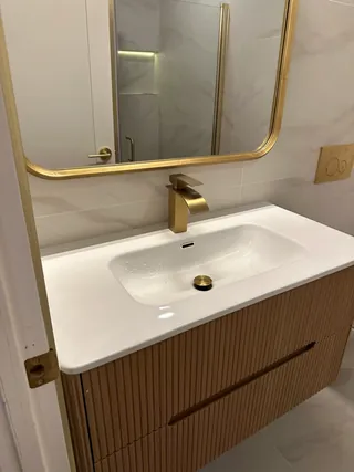 Fluted wood-tone vanity drawers below a white basin and rounded warm-metal mirror.