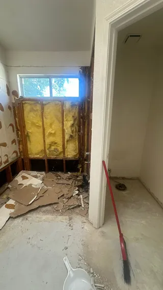 Bathroom at a stripped stage, with exposed framing and insulation beside a window and shower doorway.