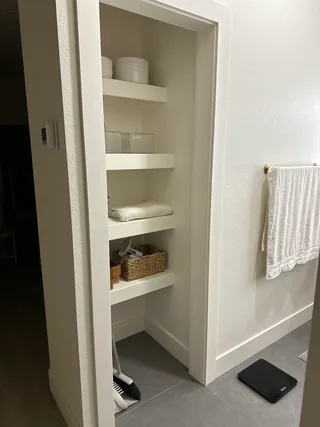 Open recessed bathroom shelving above gray rectangular floor tile, beside a white wall and towel rail.