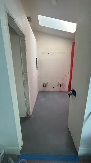 Gray rectangular floor tile beneath an empty vanity wall and bathroom skylight.