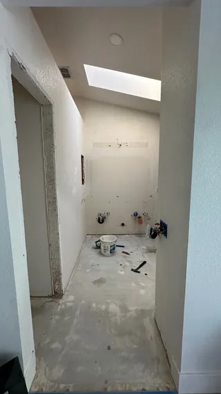 Empty bathroom vanity area beneath a skylight, with exposed service openings and an unfinished floor.