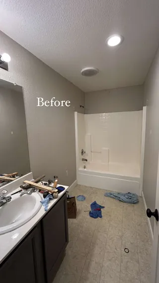 Earlier bathroom with a white bathtub surround, dark vanity and pale rectangular floor.