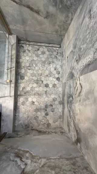 Gray and pale hexagonal mosaic shower floor beside a linear drain, tiled threshold and veined walls.