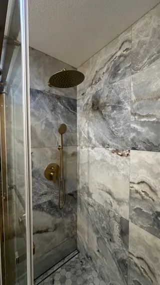 Gray-veined rectangular shower tiles meet at an inside corner beside gold-tone shower fittings.