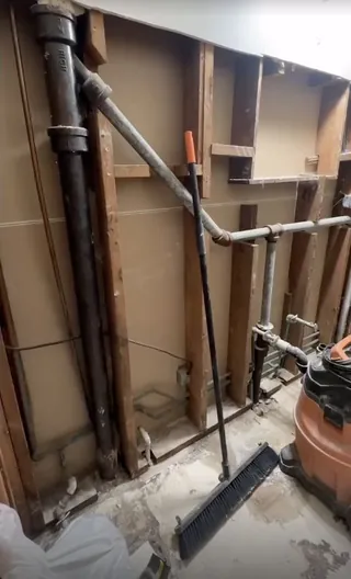 Exposed framing and pipework at a stripped bathroom vanity wall before the later tile and fittings.