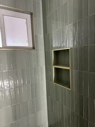 Sage vertical shower tile and a two-compartment recessed niche beside a frosted window during installation.
