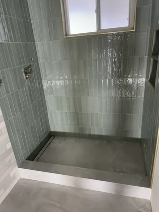Sage shower walls and pale tiled floor with a raised threshold, before shower fixtures and glass are installed.