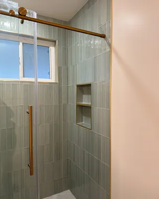 Two-compartment recessed niche with gold-tone edge trim beside a frosted shower window and vertical sage tile.