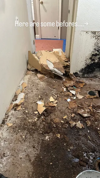 Stripped bathroom floor with demolition debris beside an exposed lower wall and doorway.