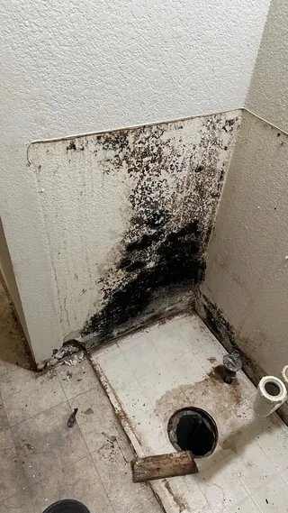 Marked lower wall beside a plumbing opening and stripped bathroom floor.