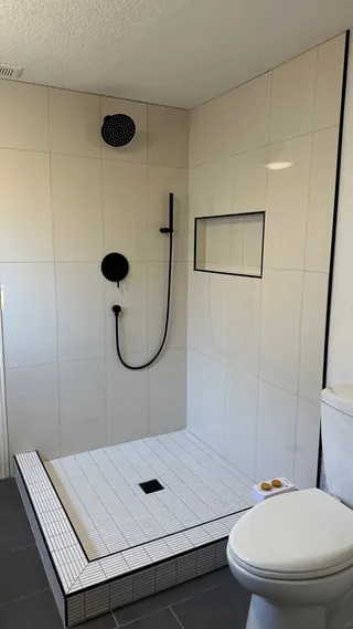White rectangular shower wall tile with black fittings and a recessed niche above slim rectangular mosaic floor tile and a square drain.
