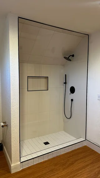 White tiled shower walls and sloping ceiling outlined by dark edge trim, with a horizontal recessed niche, black fittings and a mosaic threshold.