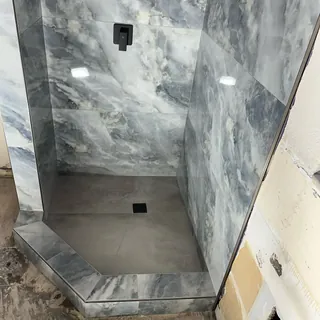 Downward view of large gray shower floor pieces, square black drain and the angled tiled threshold.