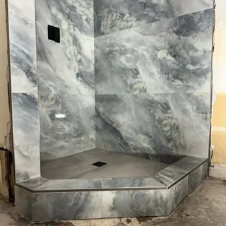 Cloudy gray-veined shower walls above an angled tiled threshold, gray floor and square black drain.