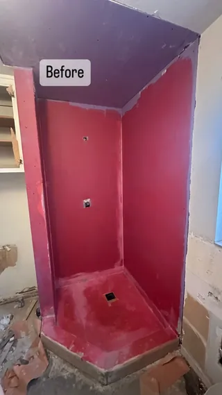 Corner shower at a red-coated preparation stage with a square drain opening and an angled raised threshold.