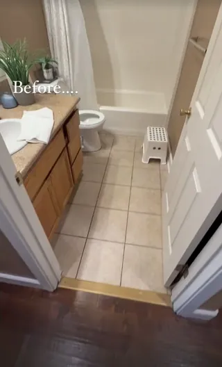 Original bathroom with a brown vanity, beige square floor tile and a white bathtub behind a shower curtain.
