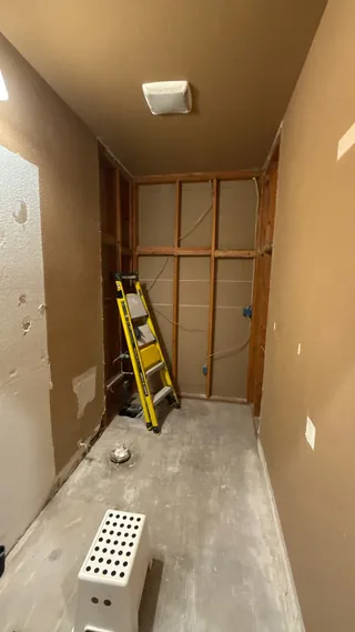 Bathroom stripped to exposed wall framing around the former tub area, with the vanity removed and bare floor visible.