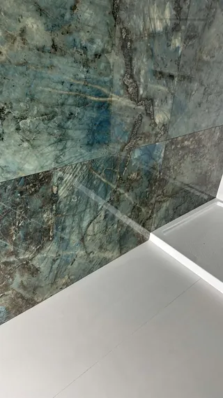 Blue-green veined wall tile meets pale floor tile beside a white shower base.