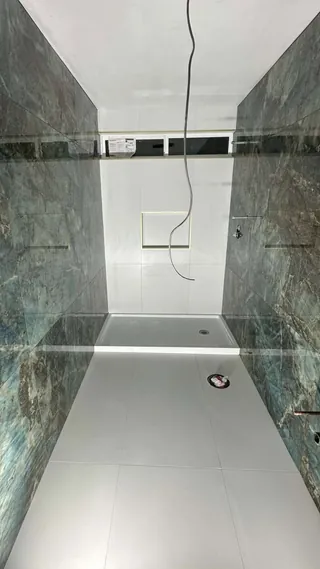 Blue-green veined side walls, white tiled end wall, high horizontal window and a white rectangular shower base.