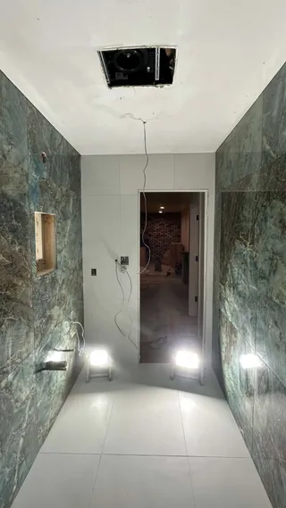 Blue-green tiled bathroom walls and pale floor tile looking toward an open doorway.