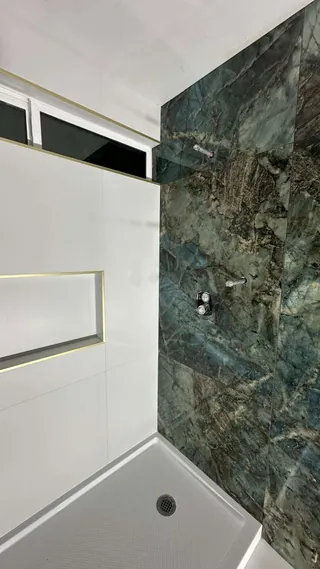 Blue-green veined shower wall beside a white tiled end wall and gold-trimmed recessed niche.