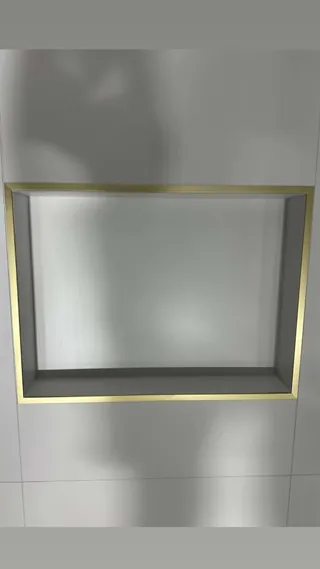 Rectangular recessed niche with gold-colored edging in a white tiled shower wall.