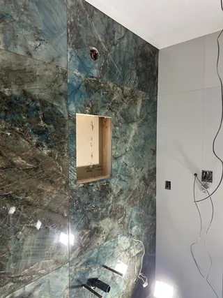 Unfinished rectangular wall recess surrounded by blue-green veined tile with exposed electrical connections.