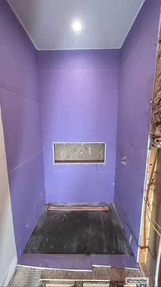 Purple board surfaces around a narrow shower with a long horizontal recessed niche and an unfinished floor area.