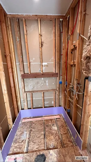 Exposed shower wall framing above a partially covered timber floor, with board pieces around the floor edge.