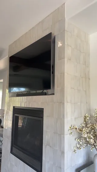 Pale glossy rectangular tiles set vertically around a black fireplace opening and recessed television, continuing around the projecting outside corner.