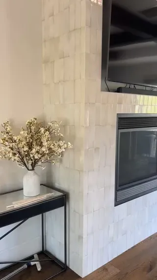Pale vertical rectangular tile around a black fireplace opening, with a recessed television above and wood-tone flooring below.