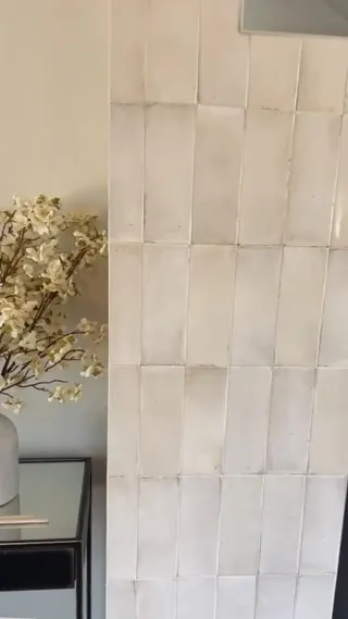 Close view of pale rectangular fireplace tile with slight cream color variation, reflective surfaces and vertical tile orientation.