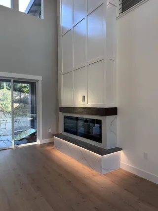 Pale veined fireplace surround and illuminated raised hearth beneath a dark mantel and tall white paneled wall.