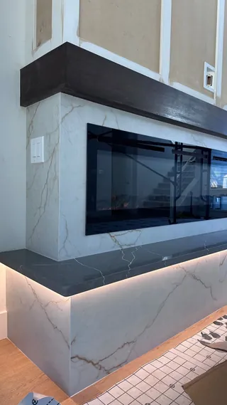 Pale veined fireplace facing, dark mantel and dark hearth ledge with warm lighting beneath.