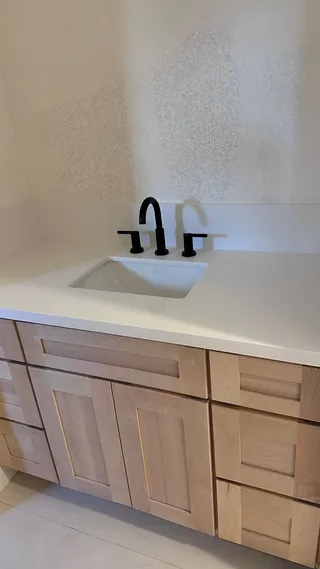 Light wood-tone vanity with framed doors and drawers beneath a white basin and black tap fittings.