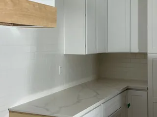 White rectangular backsplash tiles wrap a counter corner beneath white wall cabinets.