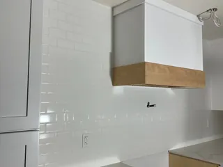 Glossy white subway tile beside a white hood enclosure with a wood-tone lower band.