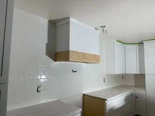 Glossy white subway tile surrounds a white box hood with a wood-tone lower band above veined counters and white cabinets.