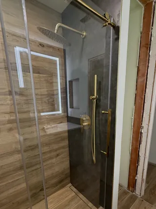 Glass shower entrance between charcoal and wood-tone tiled walls