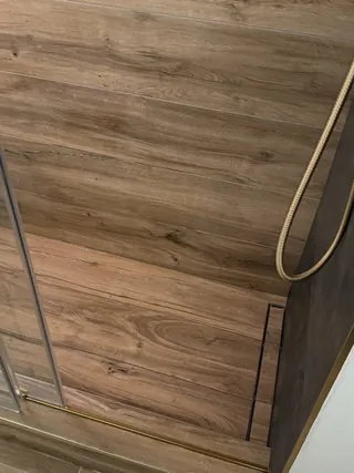 Wood-tone shower-floor tile meeting a long narrow drain and glass threshold