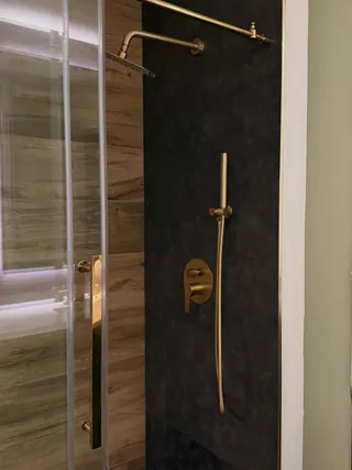 Charcoal and wood-tone shower tile with gold-tone fittings and clear glass